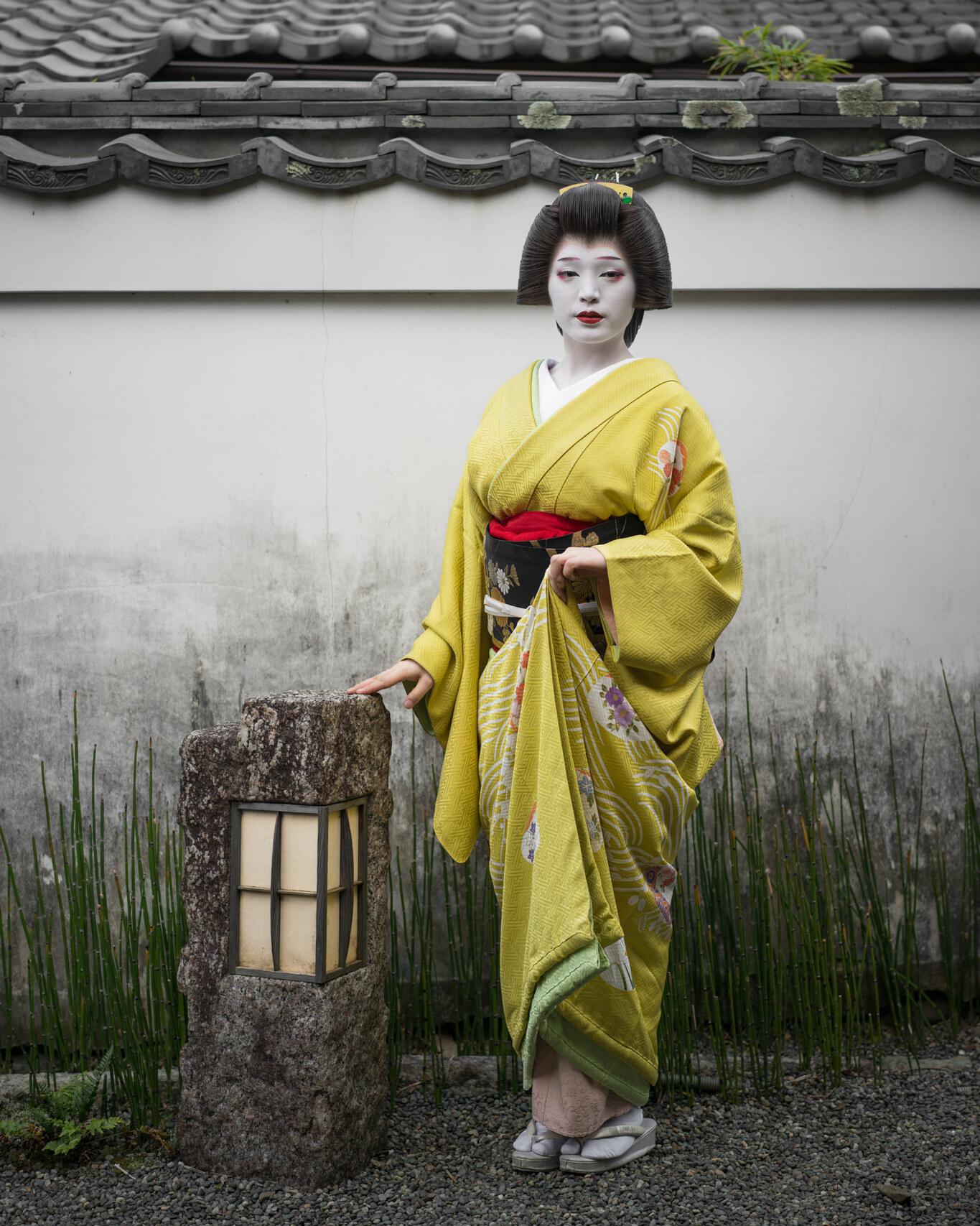 Fashion editorial portrait of a model in a yellow kimono in a Japanese garden beside a stone lantern