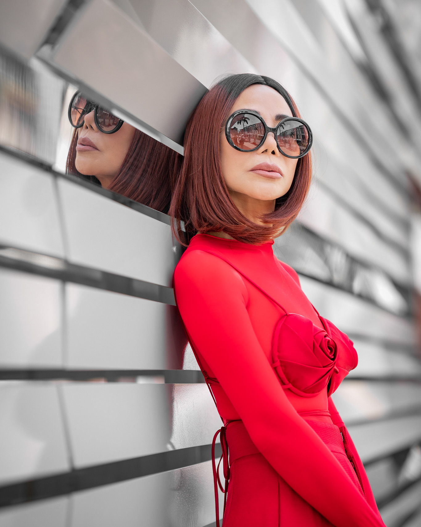 Fashion editorial model in a red look with sunglasses beside a reflective wall